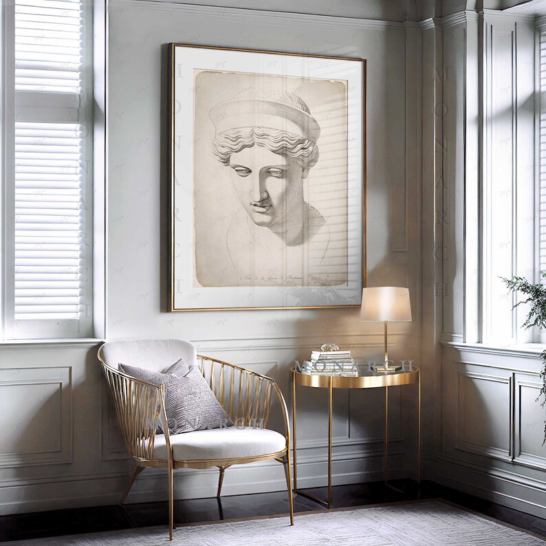 May include: A framed print of a classical bust in a gold frame hangs on a wall. The artwork is a sepia-toned sketch of a woman's face. A gold side table and chair are in front of the wall.