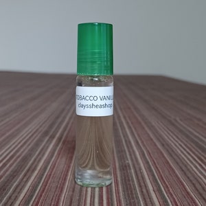 May include: A clear glass bottle with a green lid and a white label that reads "Tobacco Vanilla clayssheashop".