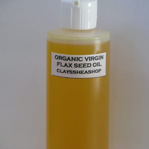 May include: A clear glass bottle with a white cap filled with yellow organic virgin flax seed oil. The bottle has a white label with the text "ORGANIC VIRGIN FLAX SEED OIL CLAYSSHEASHOP".