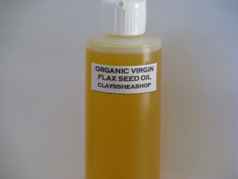 May include: A clear glass bottle with a white cap filled with yellow organic virgin flax seed oil. The bottle has a white label with the text "ORGANIC VIRGIN FLAX SEED OIL CLAYSSHEASHOP".