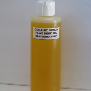 May include: A clear glass bottle filled with golden yellow organic virgin flax seed oil. The bottle has a white plastic cap and a white label with black text that reads "ORGANIC VIRGIN FLAX SEED OIL CLAYSSHEASHOP".