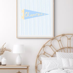 Puede incluir: Una impresión enmarcada con un banderín azul claro con las palabras "Chapel Hill NC" en amarillo. El fondo tiene rayas verticales de color azul claro. La impresión está en un marco de madera clara.