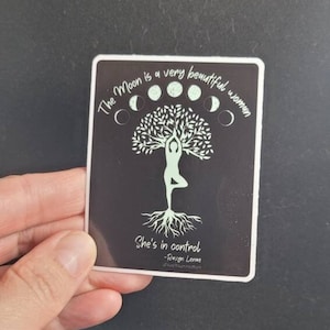 May include: A black and white sticker with a quote about the moon. The quote reads "The Moon is a very beautiful woman. She's in control -  Rumi  #moonconnection". The sticker features a tree with a woman standing on a branch, and a circle of moons around the tree.
