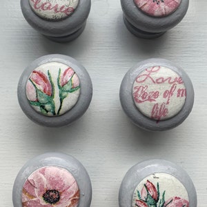 May include: Six grey round knobs with floral fabric inserts. The fabric designs include pink roses, a single pink flower, and text that reads "Eternal Love".