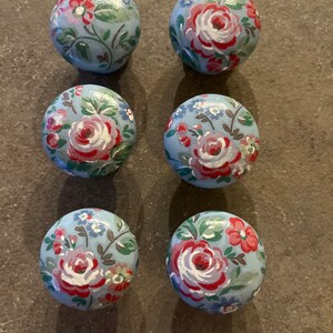 Può includere: Sei pomelli rotondi in legno con sfondo blu e un motivo floreale in tonalità rosa, rosso e verde.