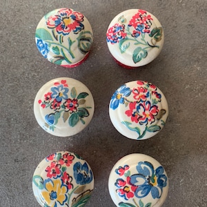 May include: Six white round knobs with a floral pattern in shades of red, blue, yellow, and green. The knobs have a red and white polka dot border.