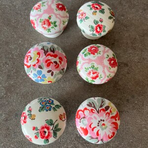 May include: Six round wooden knobs with floral patterns. The knobs are white with pink, red, blue, and green flowers.