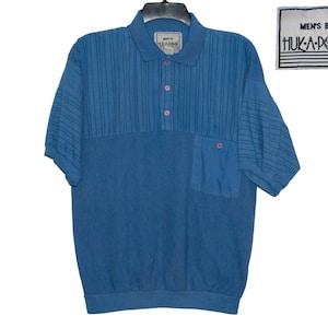 Peut inclure: Un polo bleu à manches courtes avec un motif rayé sur la moitié supérieure et une poche sur le côté gauche. Le polo a un col boutonné et une étiquette qui indique "MEN'S BY HUKA-POO TM".