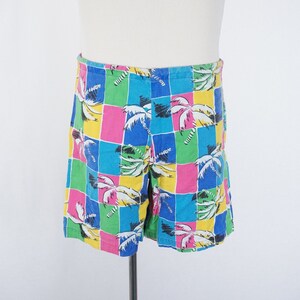May include: Colorful swim trunks with a checkered pattern featuring palm trees in shades of blue, green, pink, and yellow.