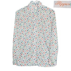 Puede incluir: Camisa blanca de manga larga con botones y estampado de labios de colores. La camisa tiene cuello y cierre de botones. El nombre de la marca "PepperTree" es visible en la etiqueta.
