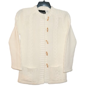 May include: A white knitted cardigan with a cable knit pattern and wooden toggle buttons.