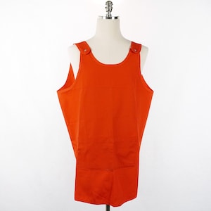 May include: A bright orange sleeveless apron with a single pocket. The apron has adjustable straps with a button closure.
