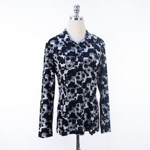 May include: A long-sleeved shirt with a black and white floral pattern. The shirt has a collared neckline and buttoned front. The pattern features dark floral shapes and vertical stripes against a light background. The shirt is displayed on a mannequin.