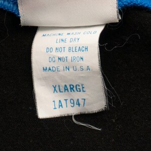 May include: White care label with black text, reading "MACHINE WASH COLD, LINE DRY, DO NOT BLEACH, DO NOT IRON, MADE IN U.S.A." Below is a white tag with black text reading "XLARGE 1AT947".