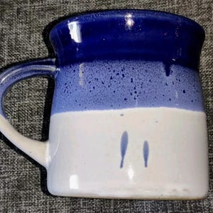 May include: A ceramic mug with a blue and white color scheme. The top of the mug is a deep blue, transitioning to a lighter blue speckled band, and then to a white base. The handle is white and blue.