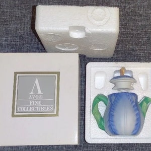 May include: A blue and green ceramic teapot in a styrofoam insert, with a matching lid and handle. The teapot is shaped like a flower. The box reads "AVON FINE COLLECTIBLES".