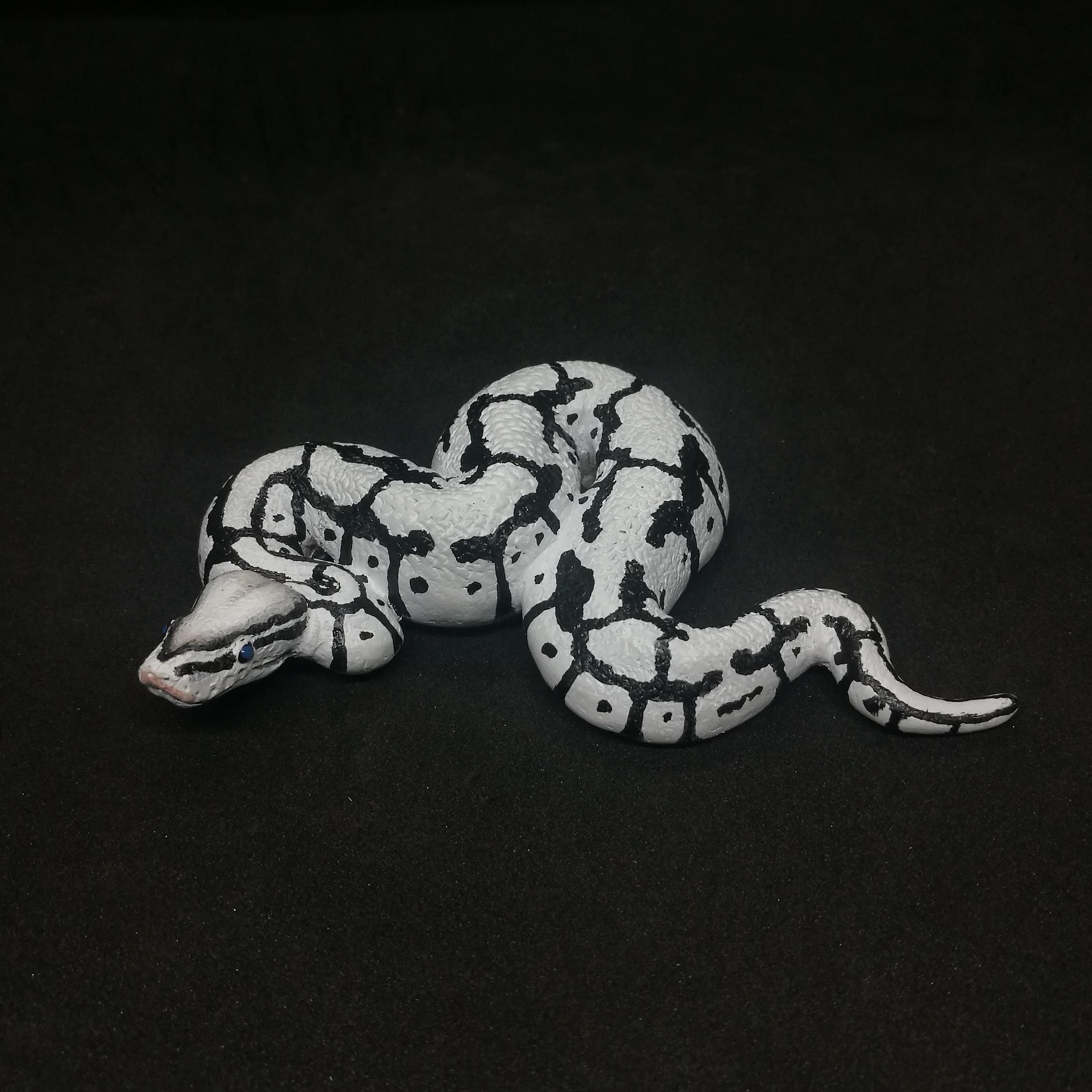 May include: A white and black snake figurine with a detailed pattern. The snake is coiled and has a realistic appearance, with a textured surface and a dark background.