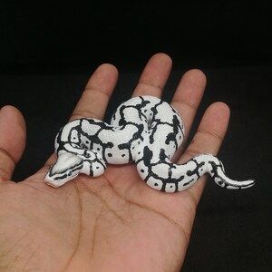 May include: A white and black patterned snake figurine. The snake is coiled and has a detailed design with black spots and markings on a white base. The snake's head is visible, with small blue accents.