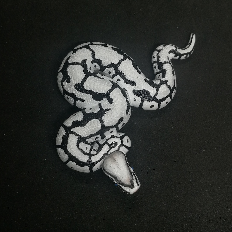 May include: A white and black decorative snake figurine. The snake is coiled with a detailed pattern of black markings on a white base. The head is triangular with a black and white pattern.