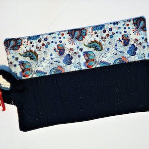 May include: A blue and white fabric pencil case with a floral pattern. The case has a black fabric lining and a zipper closure.