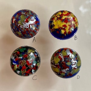 May include: Four round glass buttons with a blue base and a colourful, speckled pattern of red, yellow, green, white, and silver. The buttons are labelled A, B, C, and D.