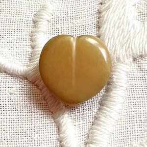 May include: A heart-shaped button made of a light brown, translucent material. The button has a smooth, glossy finish.