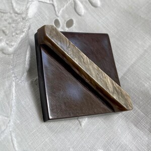 May include: A brown square brooch with a diagonal beige stripe.