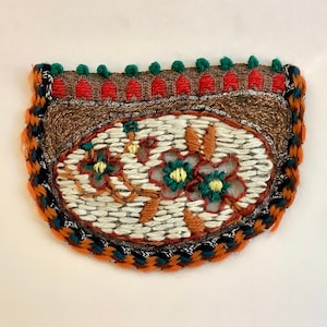 May include: A half-circle embroidered patch with a white background and a floral design in shades of orange, green, and yellow. The patch is surrounded by a brown, orange, and black braided trim.
