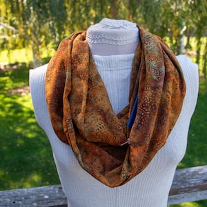 May include: A brown and green infinity scarf with a paisley pattern. The scarf is made of a soft, flowing fabric and is perfect for adding a touch of style to any outfit.