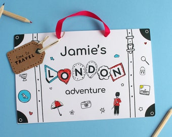 May include: A white printable sign with a suitcase design. The sign says "Jamie's London adventure" and has a brown tag that says "time to travel".