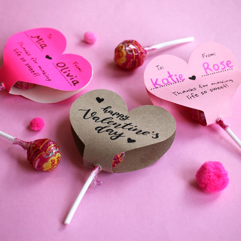 May include: Three heart-shaped lollipop holders with personalized messages. The holders are made of pink and brown paper and have a lollipop stick inserted through the bottom. The messages on the holders read "To: Mia From: Olivia Thanks for making life so sweet!"  "To: Katie From: Rose Thanks for making life so sweet!" and "happy Valentine's day".