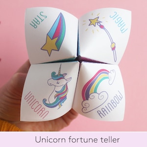 Puede incluir: Un juego de adivinanzas de papel con un diseño de unicornio, arcoíris, estrella y varita mágica. El juego de adivinanzas está doblado y se sostiene en una mano.