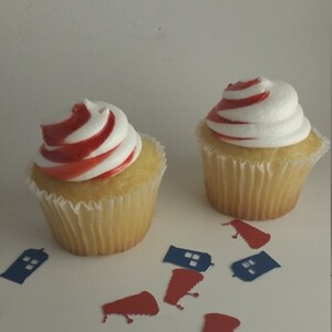 May include: Two yellow cupcakes with white frosting and red swirl designs. The cupcakes are surrounded by blue and red paper cutouts of a police box.