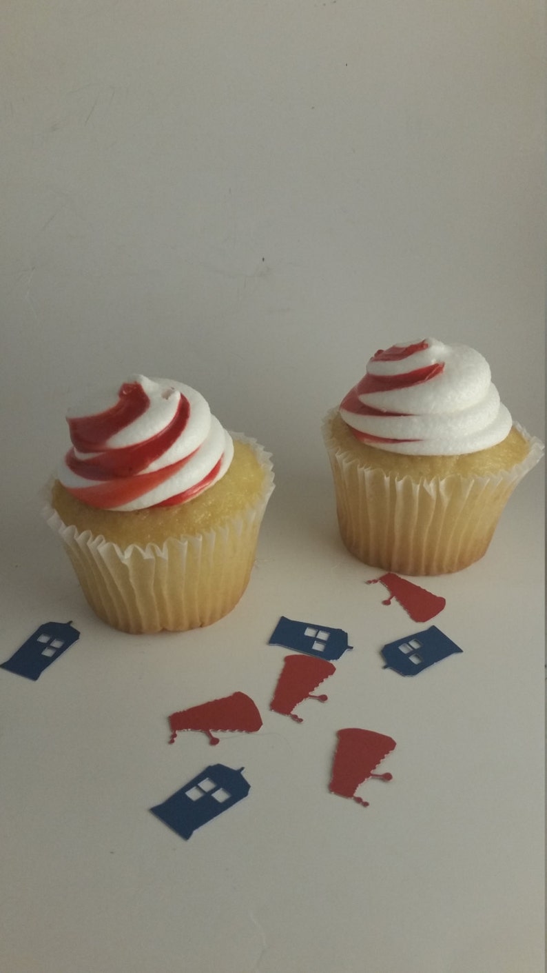 May include: Two yellow cupcakes with white frosting and red swirl designs. The cupcakes are surrounded by blue and red paper cutouts of a police box.