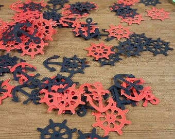May include: A scattering of red and navy blue paper confetti featuring nautical themed designs, including anchors and ship wheels. The confetti is scattered on a wooden surface.