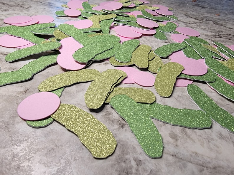 May include: A pile of green and pink glitter paper cutouts. The green cutouts are shaped like cucumbers and the pink cutouts are circles.