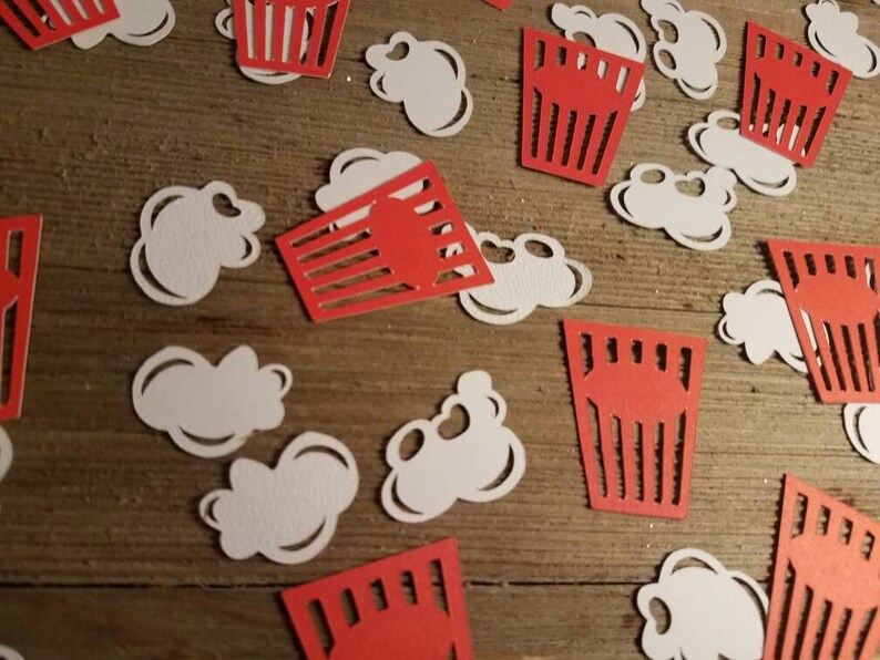 May include: Red and white paper cutouts of popcorn and popcorn boxes. The cutouts are scattered on a wooden surface.