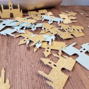 May include: A pile of gold and light blue glitter castle confetti. The confetti is shaped like castles with pointy roofs and towers.
