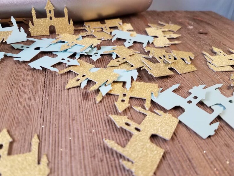 May include: A pile of gold and light blue glitter castle confetti. The confetti is shaped like castles with pointy roofs and towers.