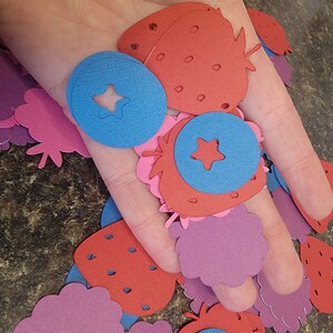 May include: A collection of paper cutouts in the shapes of strawberries, blueberries, and raspberries. The cutouts are in shades of red, pink, and blue.