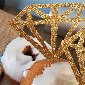 Pu&ograve; includere: Due ciambelle glassate con un topper per torta a forma di diamante con glitter dorati.