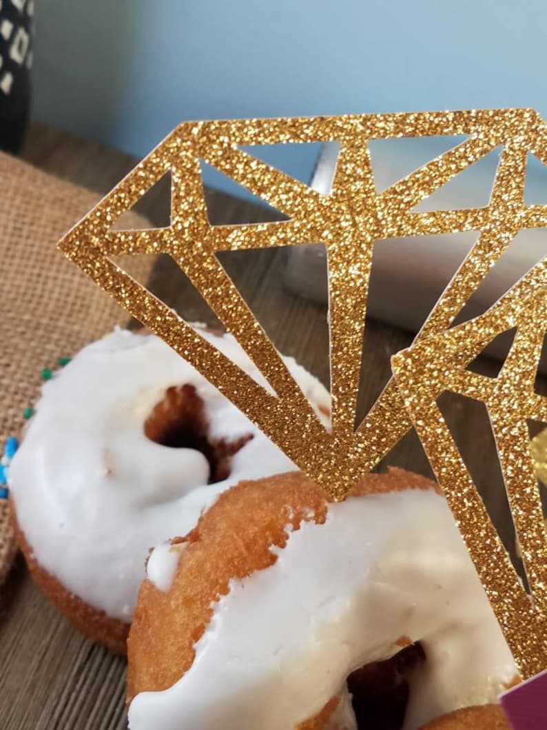 Pu&ograve; includere: Due ciambelle glassate con un topper per torta a forma di diamante con glitter dorati.