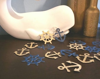 May include: A white whale figurine with blue and gold nautical themed confetti scattered around it. The confetti includes anchors and ship wheels.