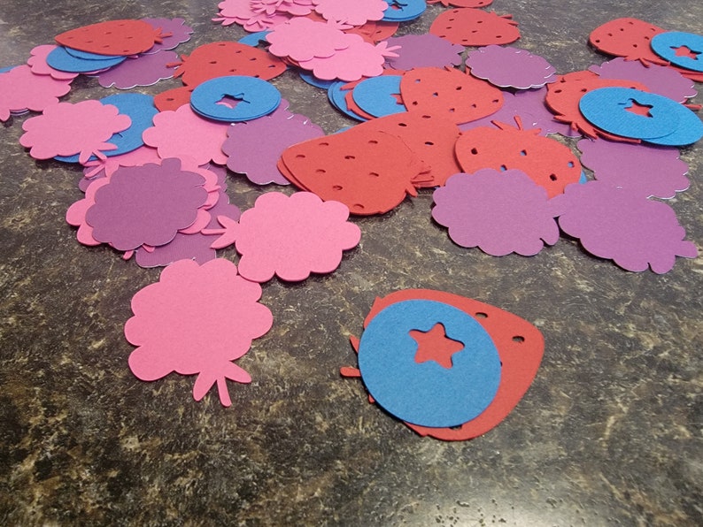 May include: Assortment of felt cutouts in pink, red, purple, and blue. The shapes include strawberries, flowers, and circles with stars.