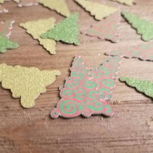 Puede incluir: Una colecci&oacute;n de adornos navide&ntilde;os de papel brillantes y festivos en varios tonos de verde y rojo. Los adornos est&aacute;n cortados en forma de &aacute;rbol de Navidad y tienen un acabado brillante y texturizado.