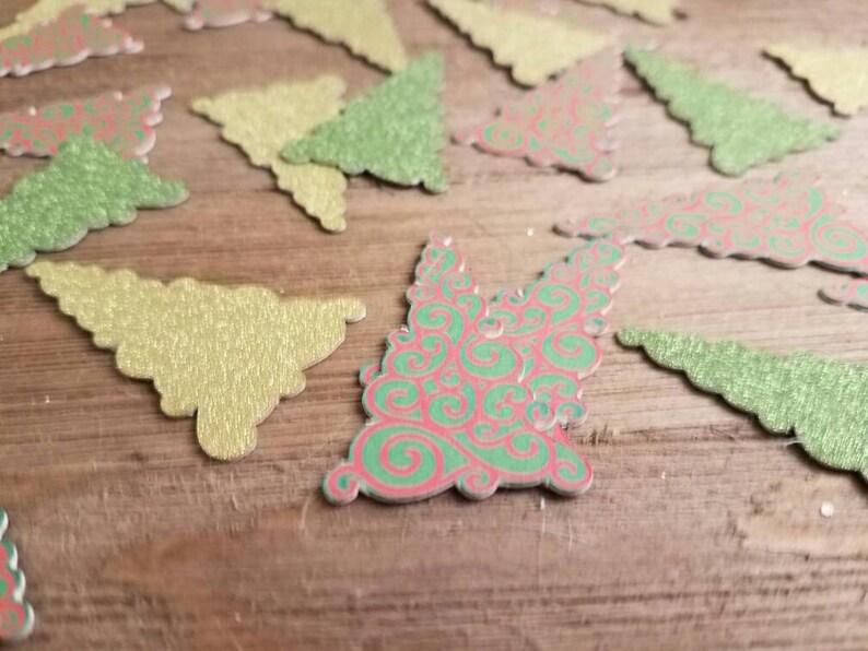 Puede incluir: Una colecci&oacute;n de adornos navide&ntilde;os de papel brillantes y festivos en varios tonos de verde y rojo. Los adornos est&aacute;n cortados en forma de &aacute;rbol de Navidad y tienen un acabado brillante y texturizado.