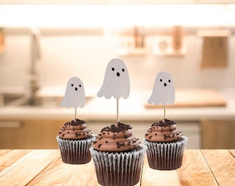 May include: Three chocolate cupcakes topped with white frosting and decorated with glitter ghost cupcake toppers.
