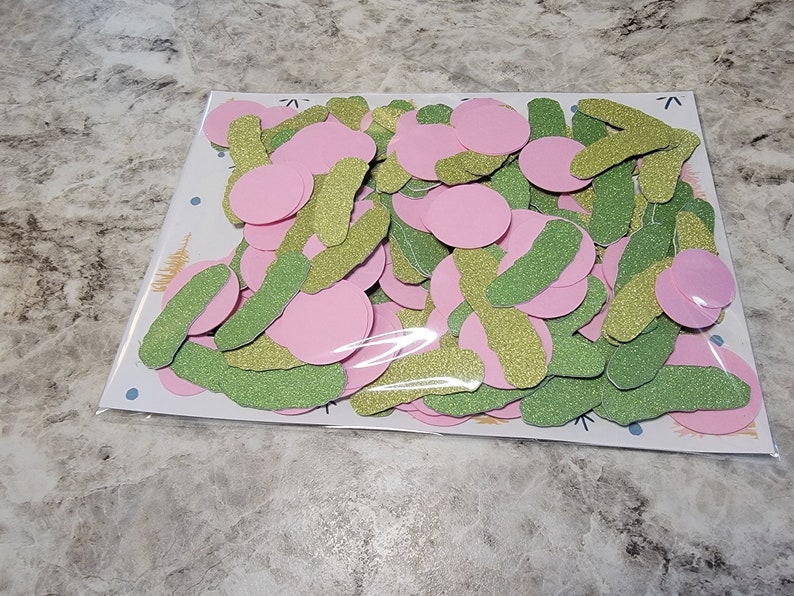 May include: A bag of pink and green glitter confetti. The confetti is in the shape of circles and long, thin rectangles.