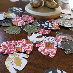 May include: Assortment of colorful paper cutouts in the shape of mittens. The cutouts feature various patterns including red and white, black and white, and green and gold.