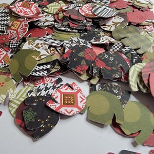 May include: A large pile of colorful paper cutouts shaped like sweaters. The cutouts feature various holiday patterns, including plaid, snowflakes, and geometric designs.